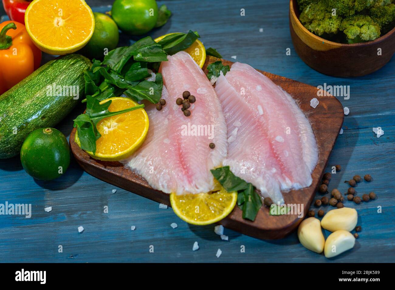 Filetto di pesce con arancia, sale di grano, pepe e spinaci, su una base di legno blu, pronto per cucinare. Foto Stock