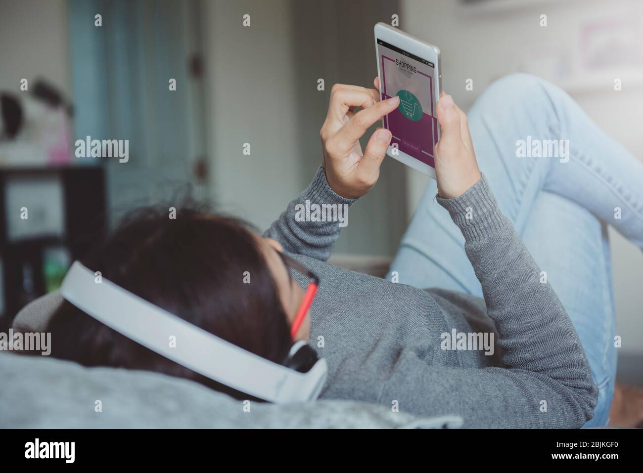 Giovane donna che utilizza lo smartphone per acquistare acquisti online mentre si trova sul divano quando si è rilassati nel soggiorno di casa. Lo shopping online e lo stile di vita moderno concep Foto Stock