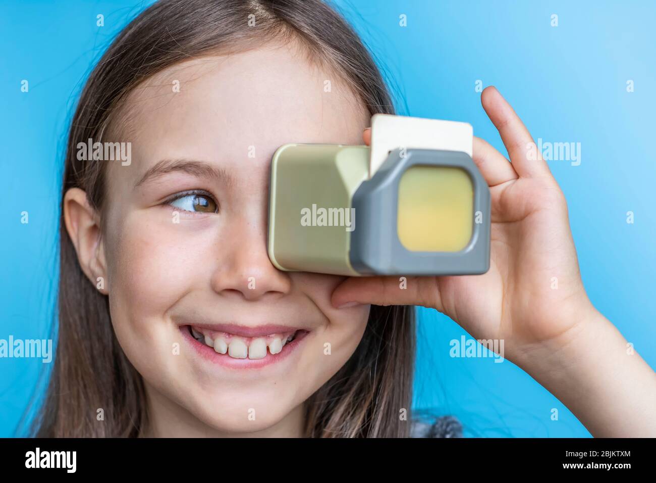 Sorridente bambina guarda vecchie foto attraverso un diascope. Modello banner su bg blu. Foto Stock