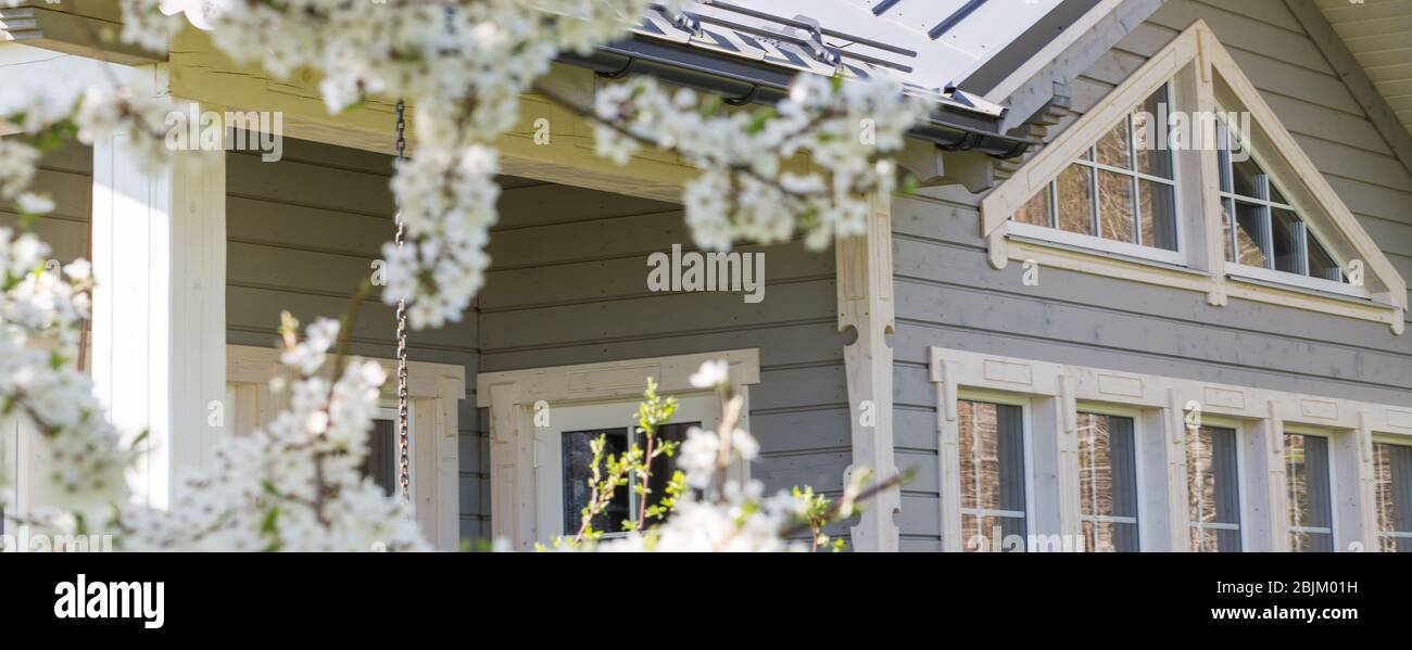 Bella casa in legno con grandi finestre, una vetrina e una terrazza sullo sfondo di alberi primaverili fioriti Foto Stock