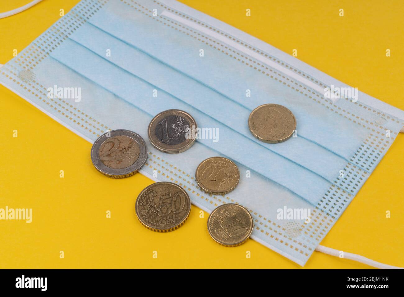 Una maschera chirurgica e alcune monete in euro. Foto Stock