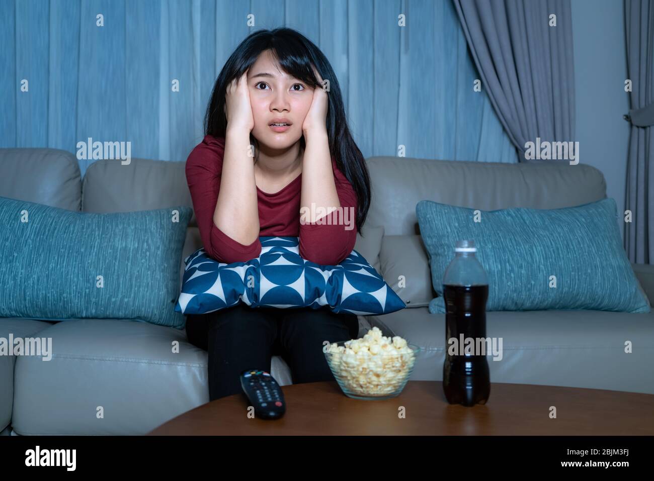 Giovane donna asiatica che guarda la televisione sospende film o notizie che guardano scioccato ed eccitato mangiare popcorn tarda notte a casa soggiorno divano durante ti Foto Stock