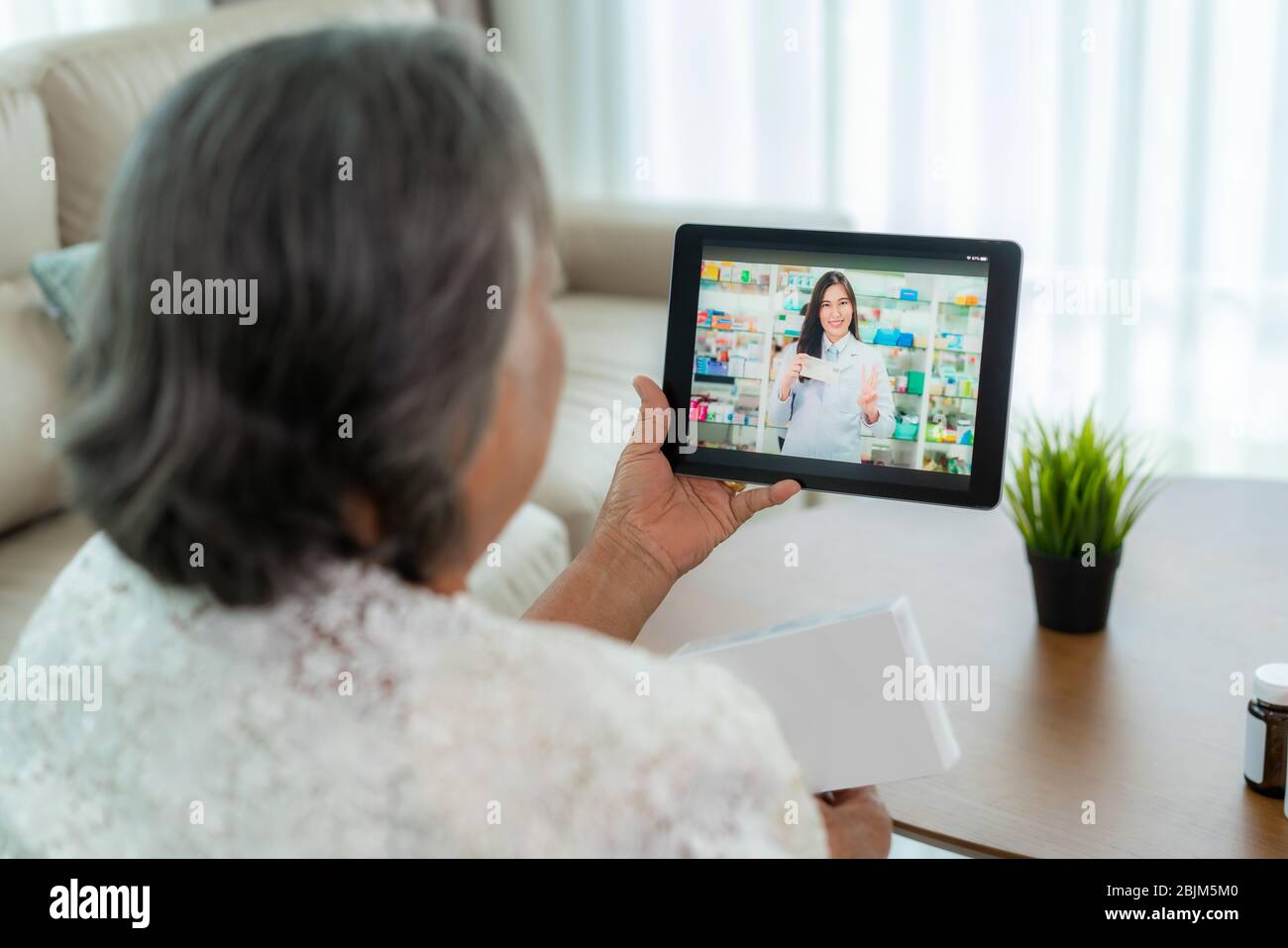 Donna anziana asiatica usando la video conferenza, faccia la consultazione in linea con la farmacia che consulta circa la malattia e la medicina via video chiamata. Telelavoro, Foto Stock
