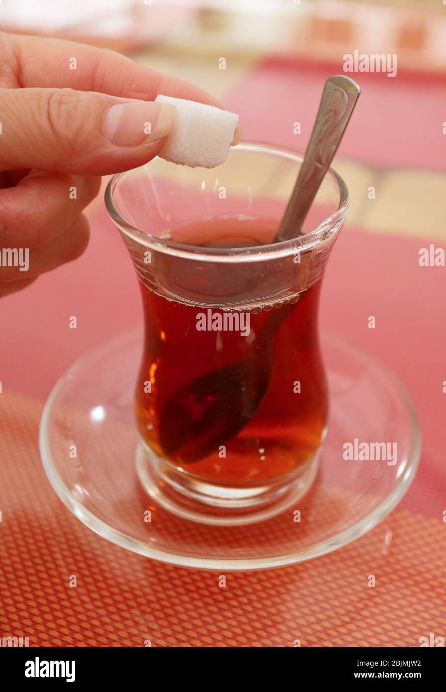 Mano della donna che fa cadere un Cubo di zucchero nel bicchiere di tè turco Foto Stock