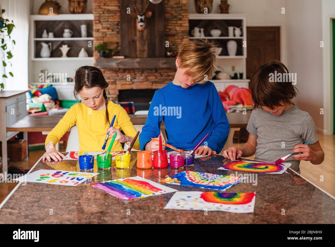 Tre bambini seduti in cucina dipingendo un arcobaleno Foto Stock