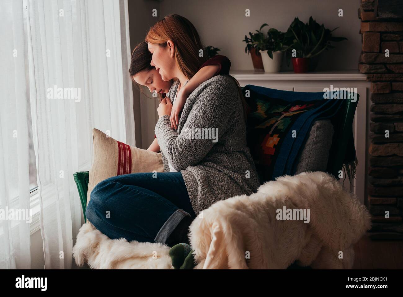Ragazza che abbracciava la madre seduta su una poltrona Foto Stock