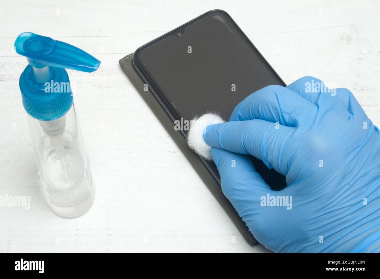 Mano umana in uno smartphone di pulizia con guanti protettivi con liquido disinfettante su fondo bianco. Foto Stock