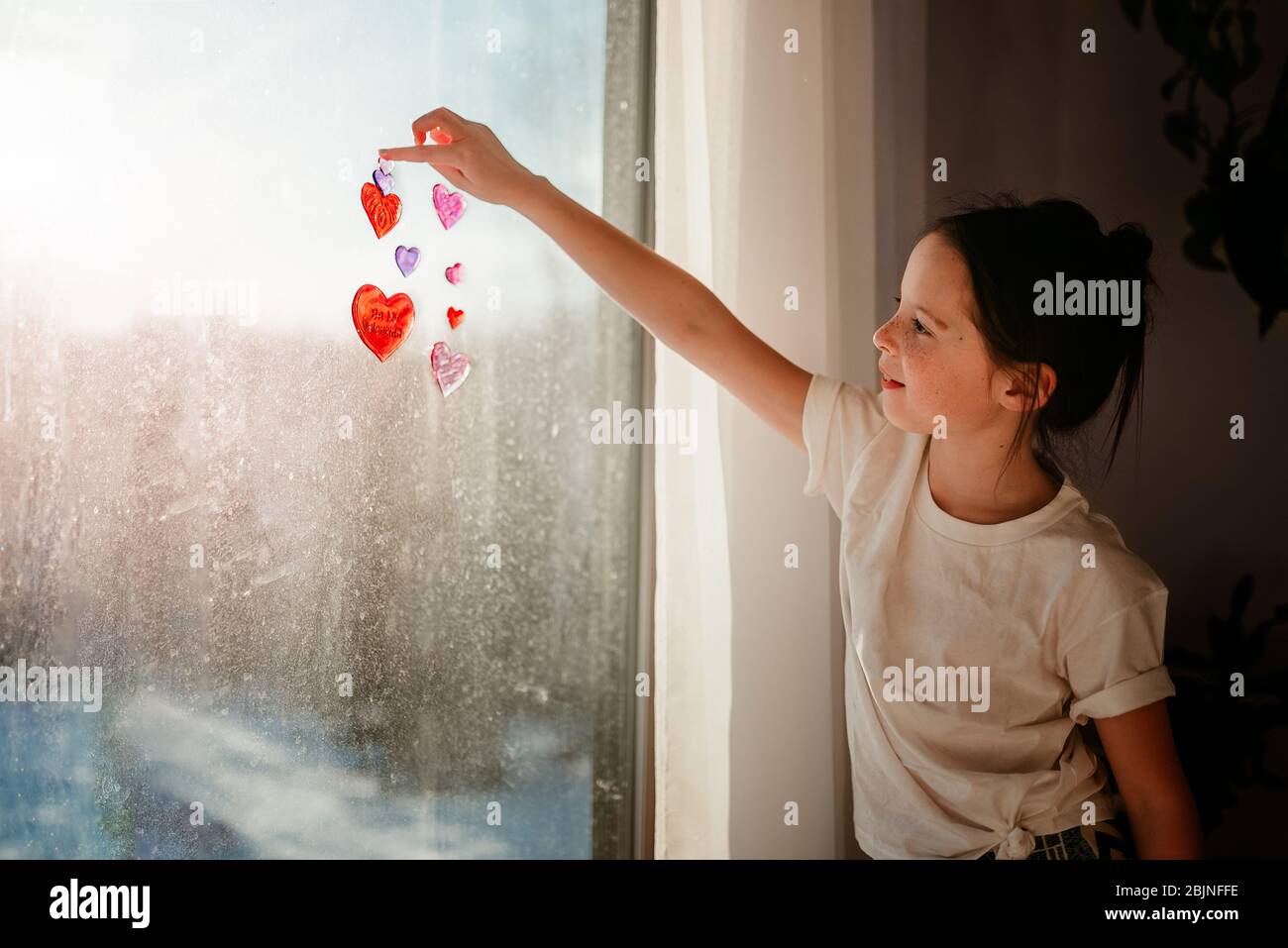 Ragazza che si attacca le decorazioni del cuore su una finestra Foto Stock
