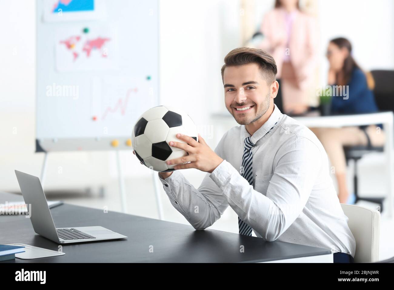 Giovane bell'uomo con palla da calcio in ufficio Foto Stock