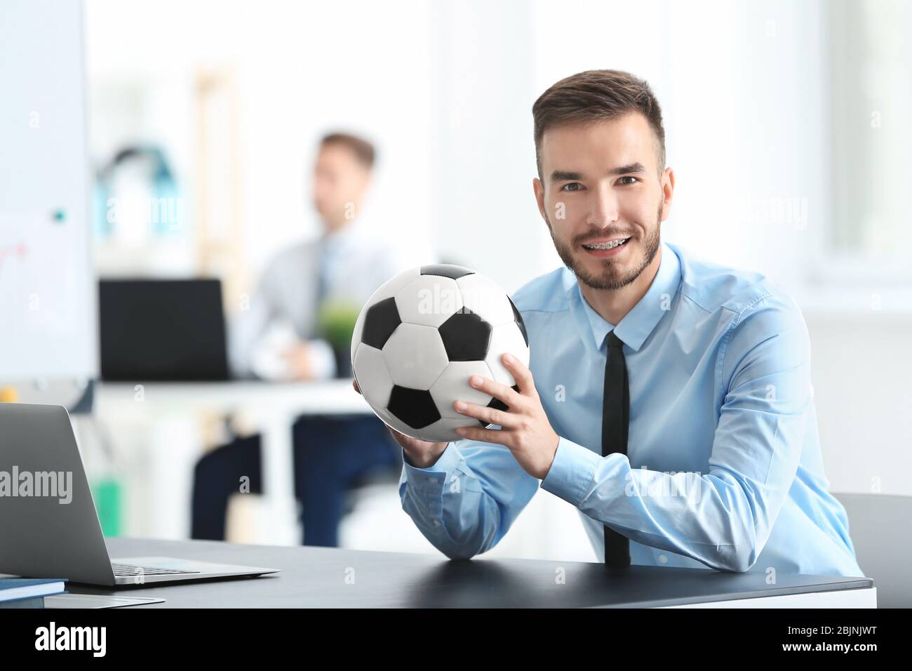 Giovane bell'uomo con palla da calcio in ufficio Foto Stock