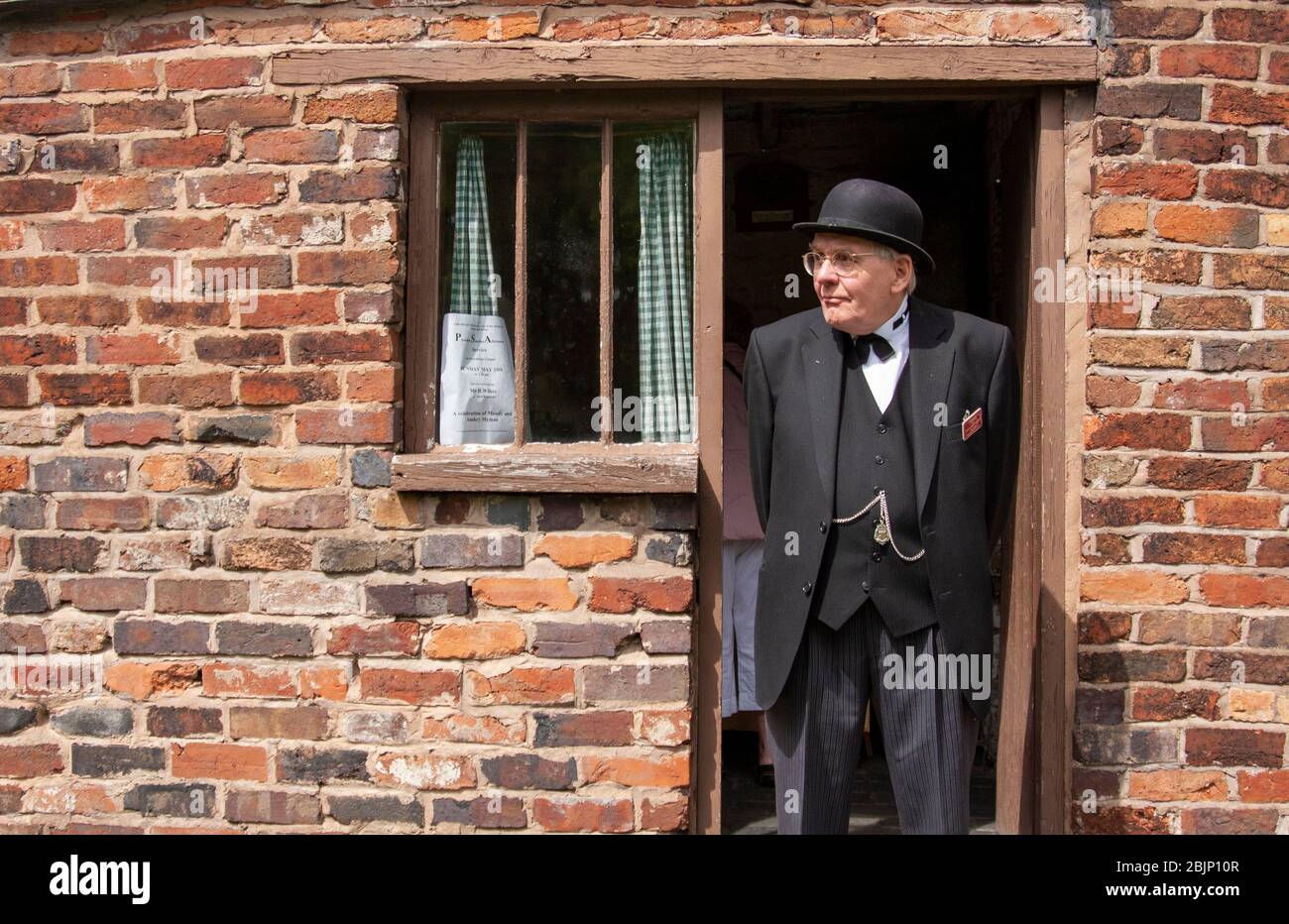 Uomo anziano, vestito con autentici abiti degli anni '40, si trovava nella porta posteriore di una casa di mattoni rossi. Birmingham, Inghilterra, Regno Unito Foto Stock
