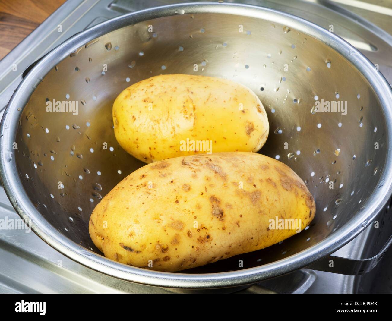 Due grandi patate bianche lavate in un colapasta di acciaio inossidabile su uno scolo da cucina Foto Stock