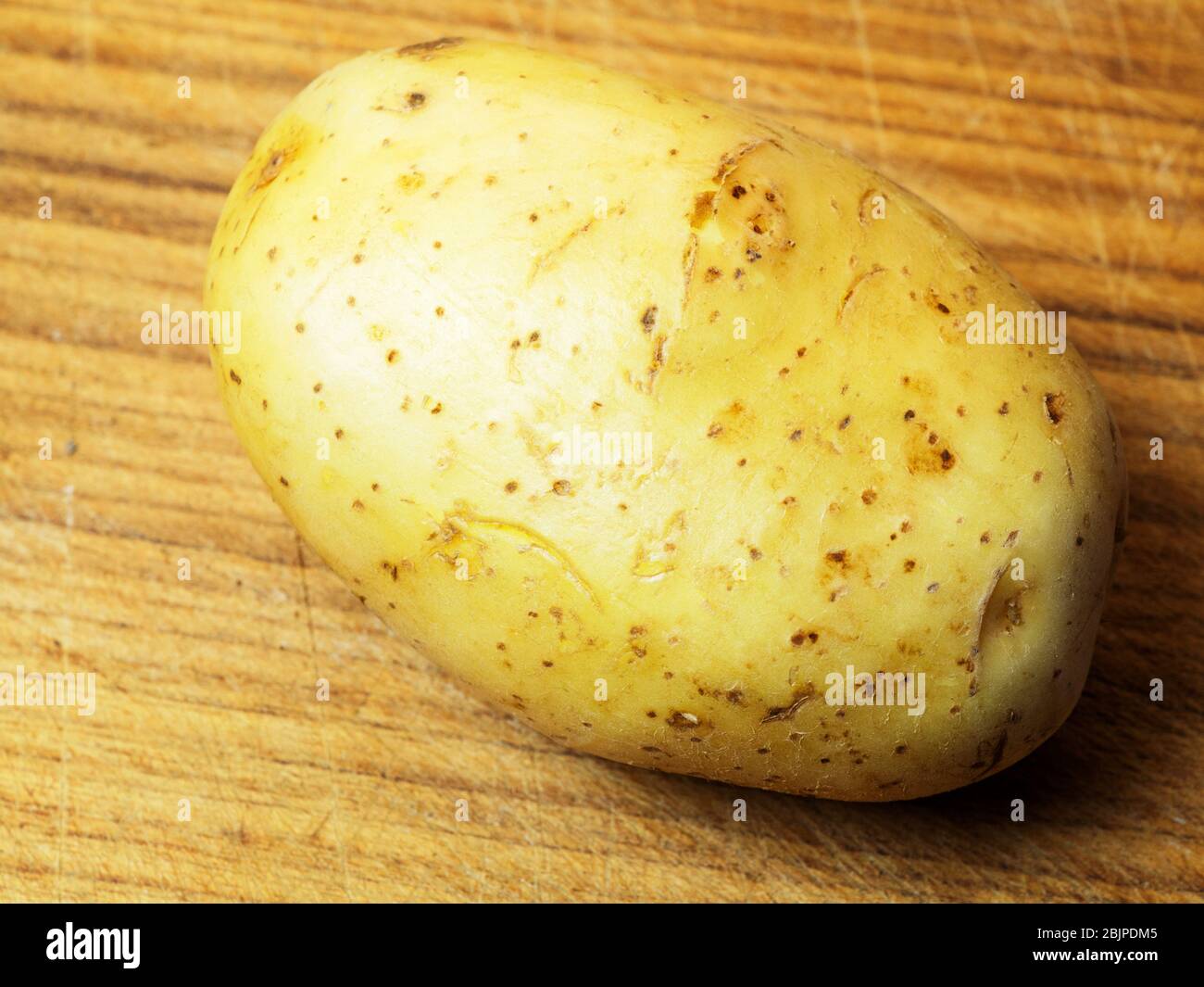 Una patata bianca intera con pelle su un tagliere di legno Foto Stock