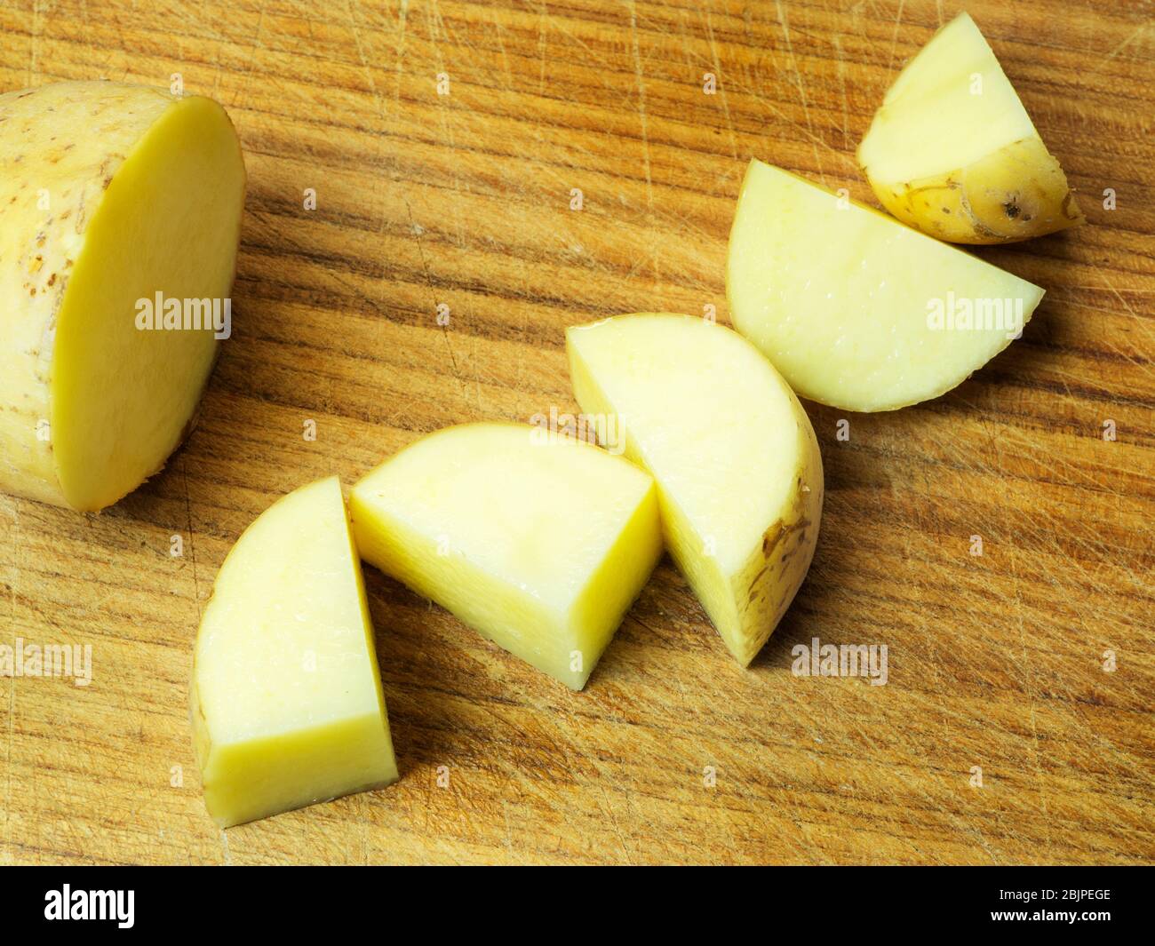 Una patata mezzo bianca e cinque pezzi di patate con la pelle su un tagliere di legno Foto Stock