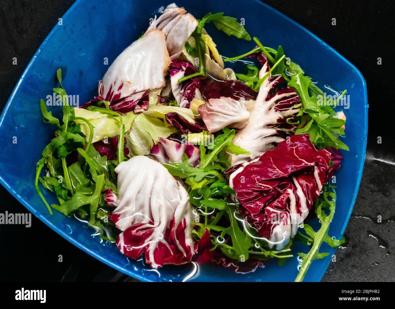 Lavare con acqua la rucola e l'insalata di lattuga nel piatto di plastica blu da vicino. Foto Stock