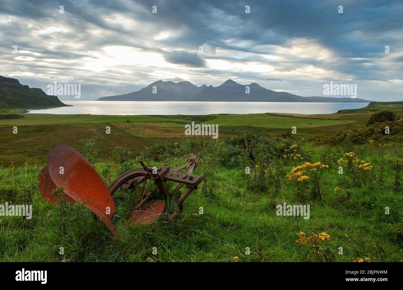 Un vecchio aratro in un campo sull'isola di Eigg con le montagne di Rum oltre. Le isole fanno parte delle piccole isole, le Ebridi interne, la Scozia. Foto Stock
