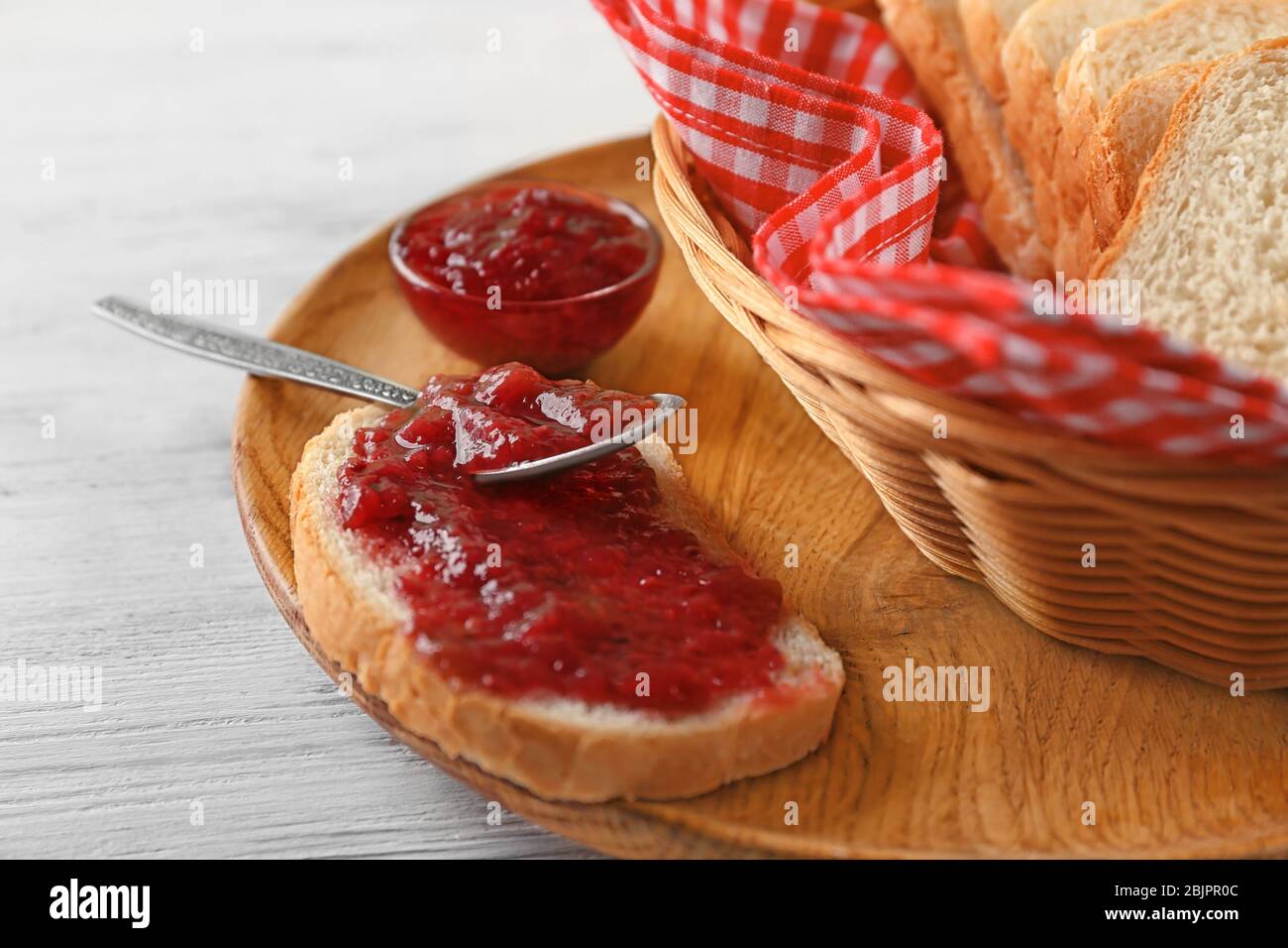 Pane con marmellata di fragole su piastra di legno Foto Stock