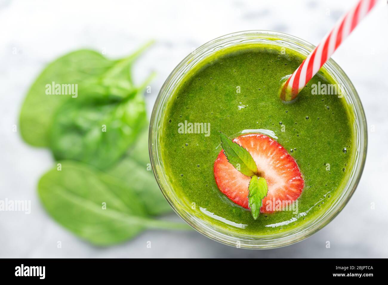 Vista dall'alto di un frullato di spinaci verdi con cornice di fragola e lime e una paglia da bere a righe rosse Foto Stock