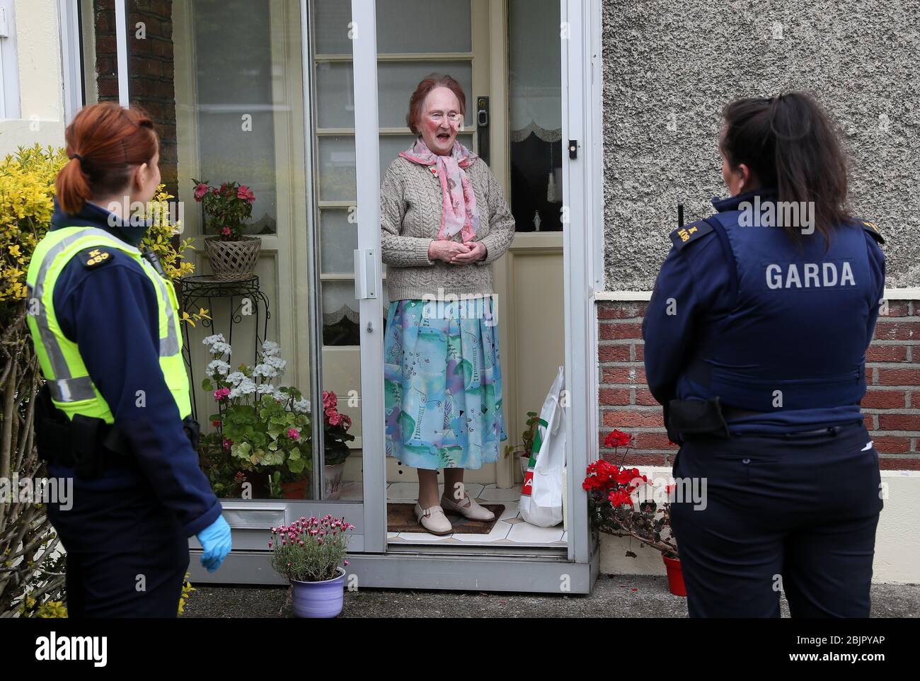 Paula McCadden, di Ballygall, riceve i suoi acquisti dalla Community Garda Louise o'Sullivan (a destra) e dalla probaioner Garda Anna Szczepan. I membri di un Garda continuano a impegnarsi in un'ampia gamma di attività comunitarie, nel tentativo di aiutare le persone attraverso la pandemia del Covid-19, compresa la fornitura di medicinali per autoisolamento, la raccolta di pensioni, e fare lo shopping per la gente coconooning. Foto Stock