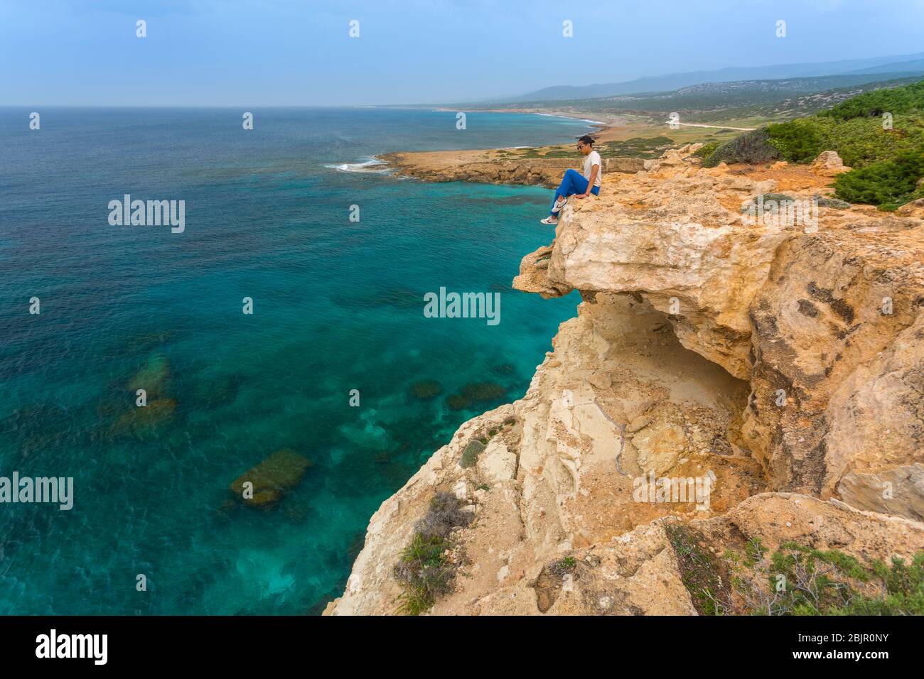 Giovane seduto sul bordo di una scogliera che si affaccia sull'oceano a Lara Beach sulla penisola di Akamas, Cipro Foto Stock