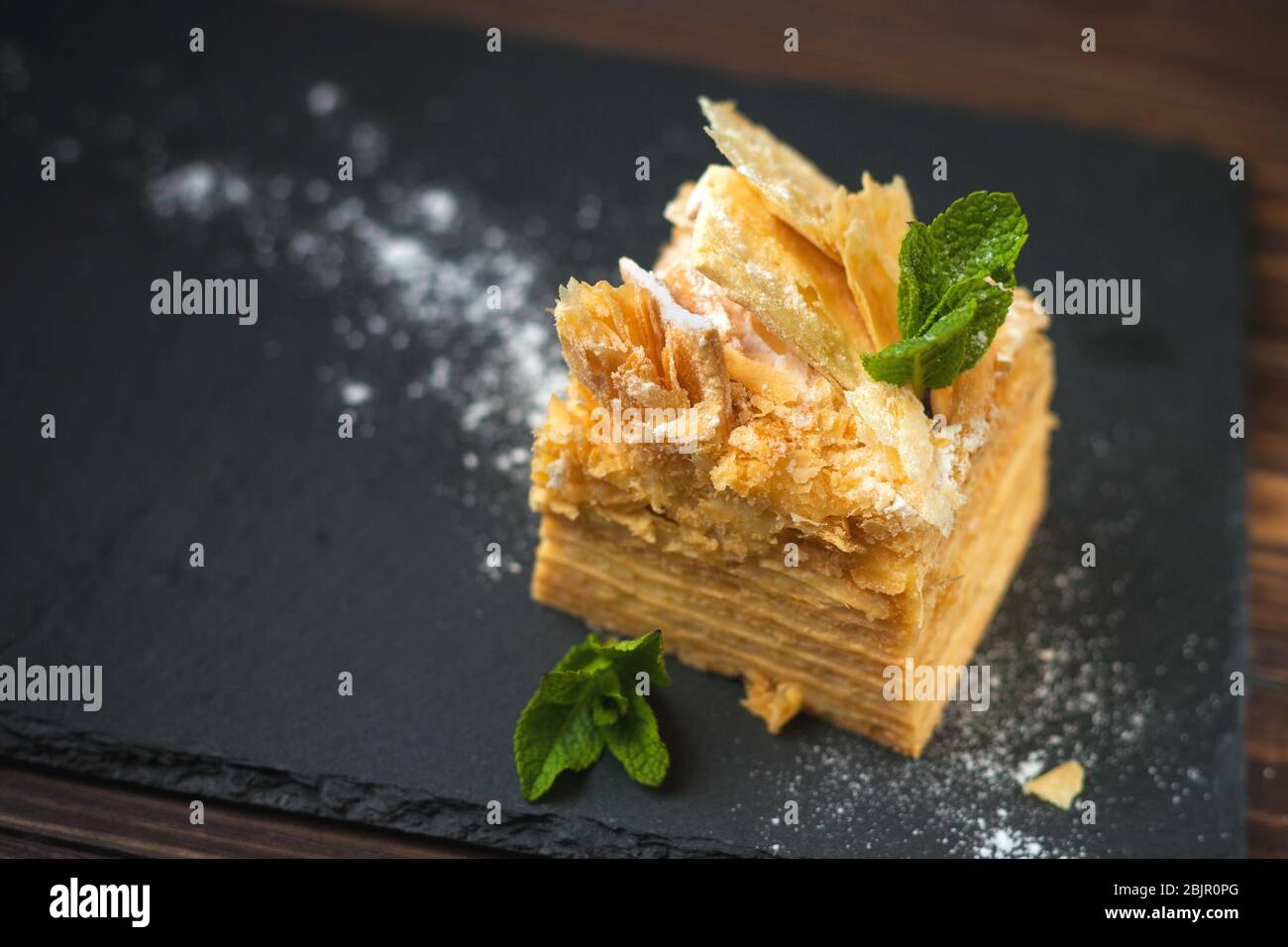 Torta di Napoleone con crema pasticcera e foglie di menta. Per il menu del cafe'. Area di testo per la progettazione. Con sfondo nero. Foto Stock