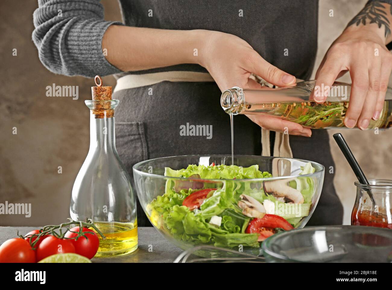 Donna che aggiunge gustoso condimento per insalata in piatto sul tavolo Foto Stock