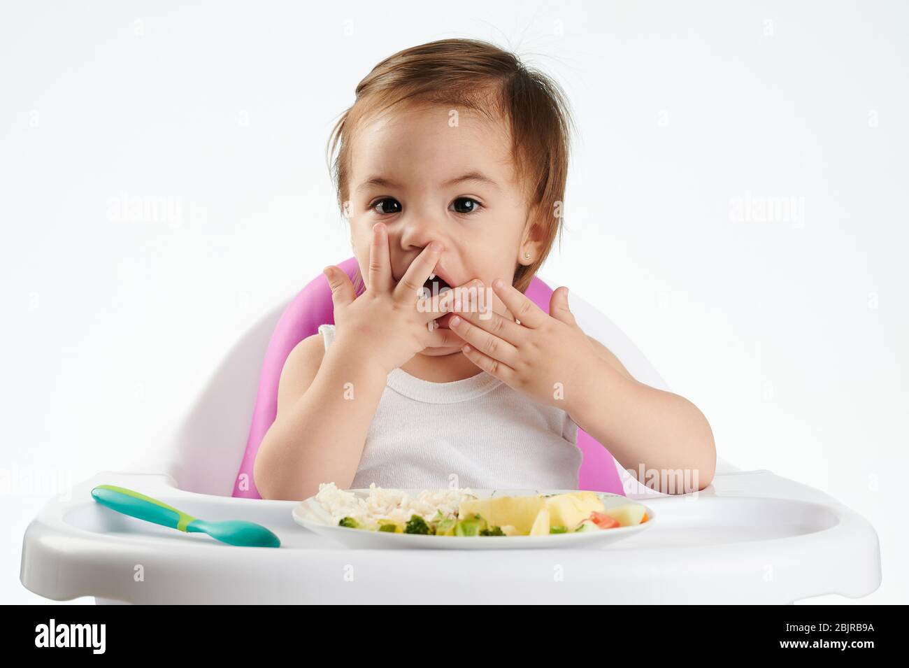 Il bambino mangia con le mani su un seggiolone isolato su sfondo bianco Foto Stock
