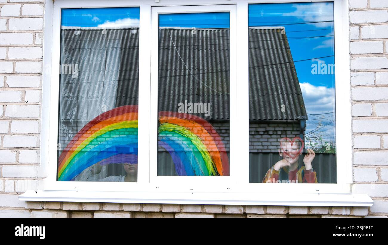 Ragazzo vicino alla finestra, arcobaleno, fine della quarantena. Un ragazzo disegna un arcobaleno e un cuore rosso. Il concetto di inseguimento dell'arcobaleno Foto Stock