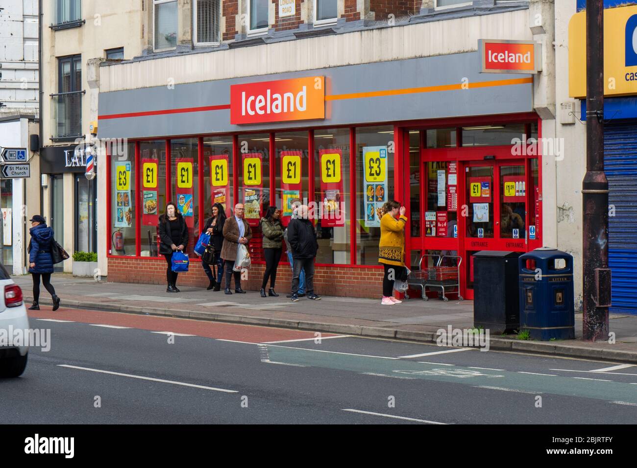 Gli acquirenti che effettuano le distanze sociali mentre fanno la coda fuori di un supermercato Islanda durante la pandemia del covid-19 Foto Stock