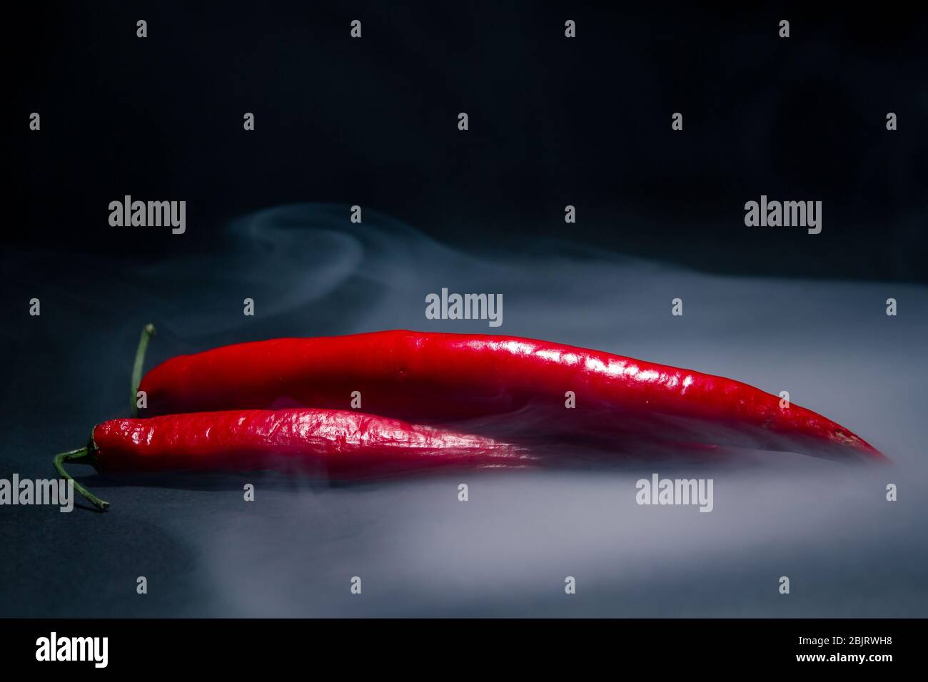 due peperoni rossi caldi fumati su sfondo scuro sotto la luce di uno spazio di copia sotto i riflettori Foto Stock