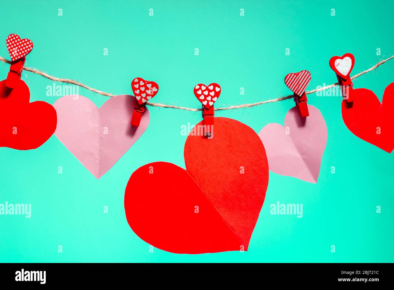 Cuori di carta di clothespins rossi con un cuore su una corda. San Valentino amore. Sfondo Aqua Menthes. Spazio di copia Foto Stock