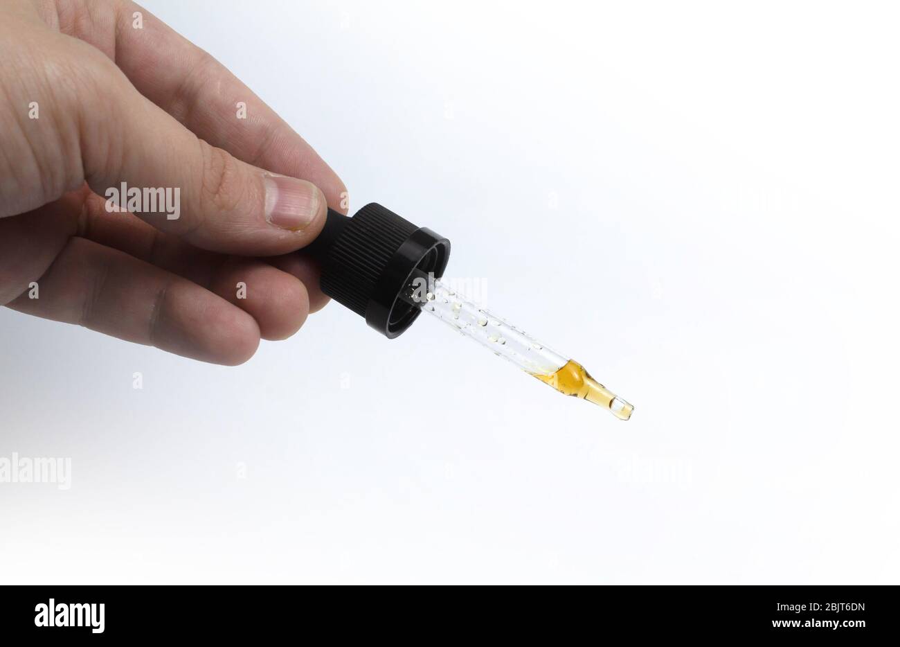 Contagocce con liquido scuro in mano su un isolato di fondo bianco Foto Stock