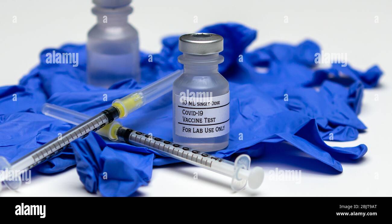 Un paio di flaconcini per vaccino di prova Covid-19 sopra i guanti per uso medico in gomma blu. Foto Stock