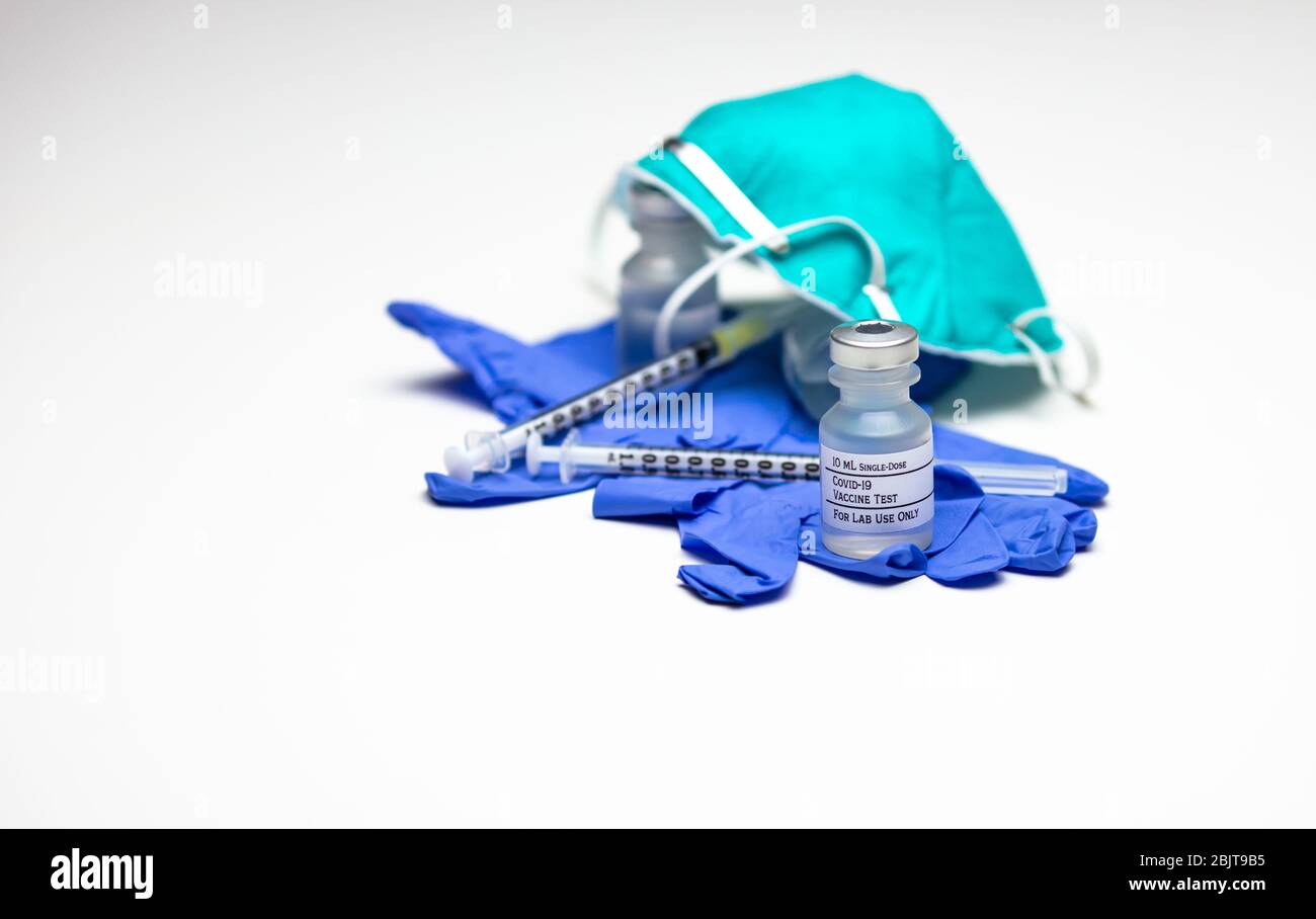 Due siringhe sopra i guanti blu per uso medico con due flaconcini di vaccino Covid-19 Test e una maschera per respiratore. Foto Stock
