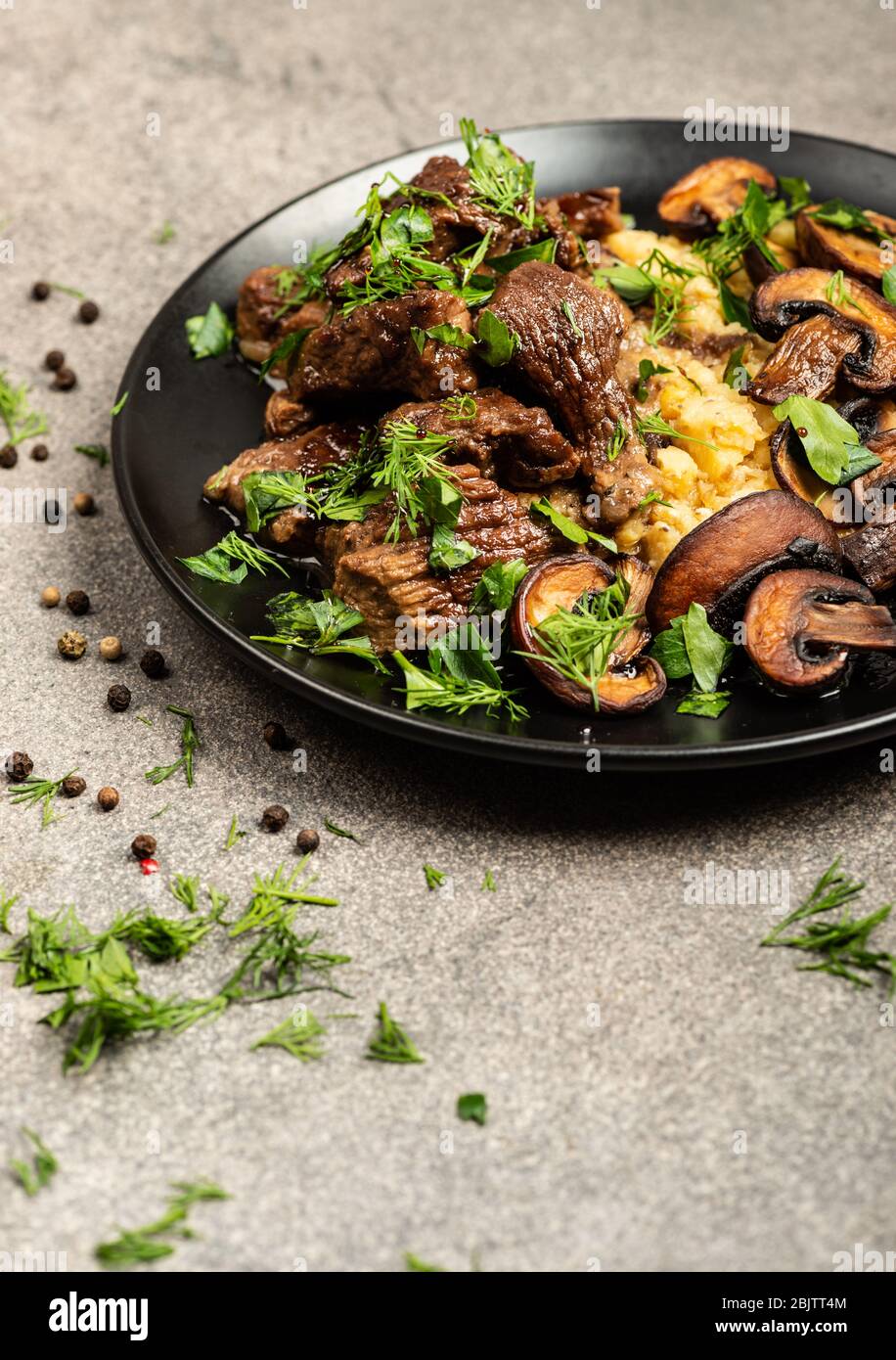 Stufato di manzo con funghi e un contorno di lenticchie su un piatto nero. Primo piano Foto Stock