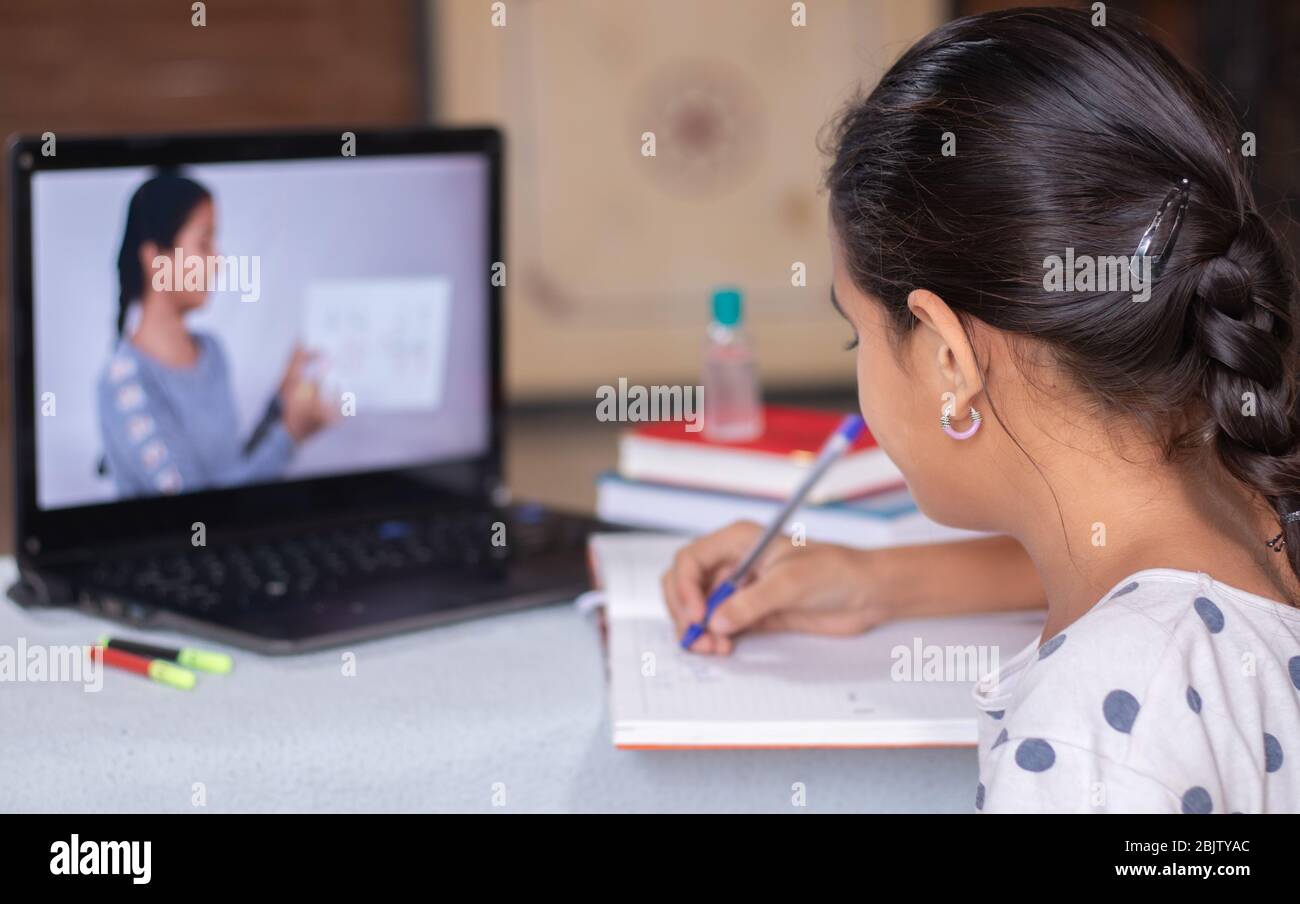 Concetto di homeschooling o e-learning, giovane ragazza impegnata a scrivere guardando il laptop mentre l'insegnante spiega durante il covid-19 o coronavirus Foto Stock