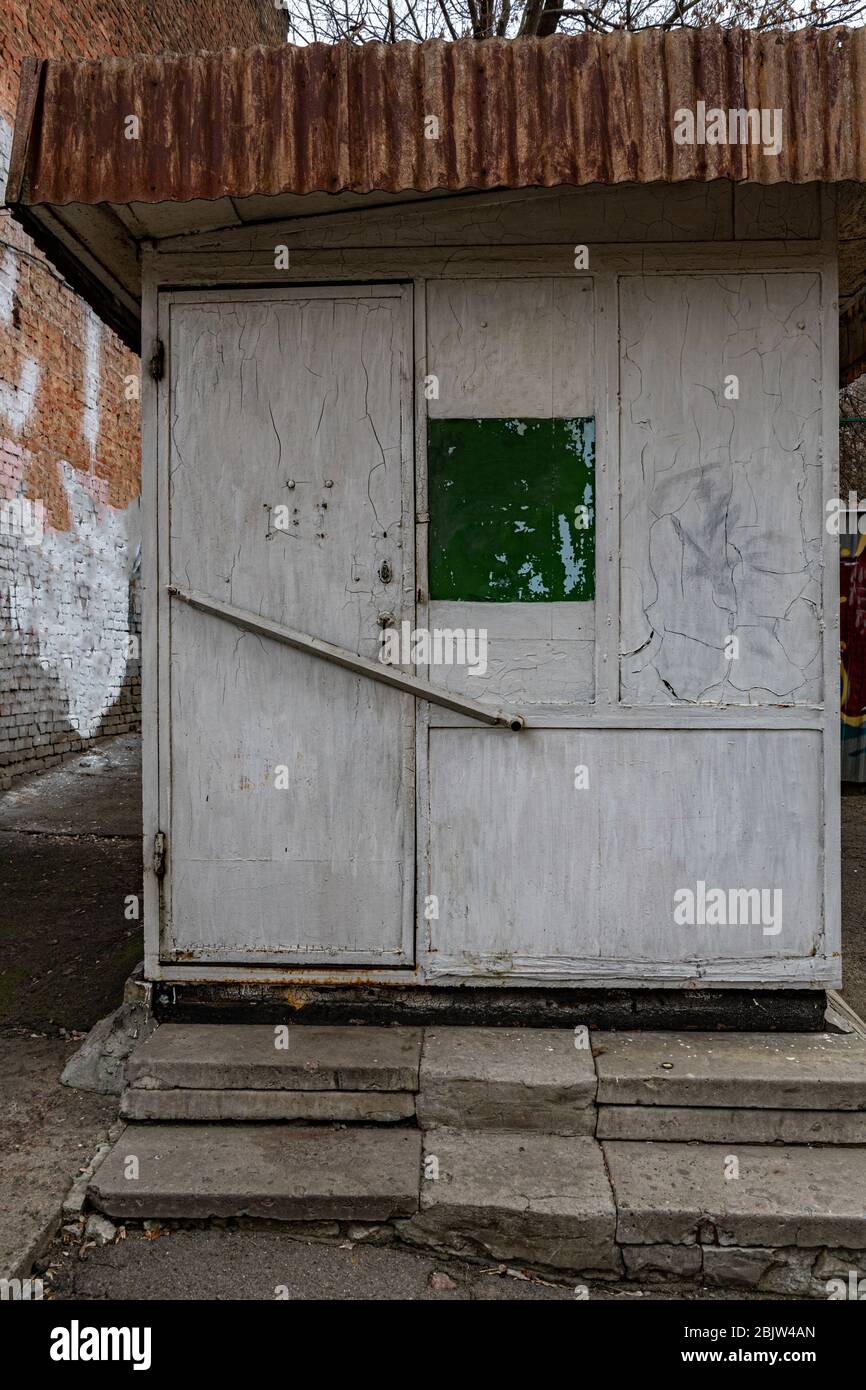 Vecchio stallino di officina di scarpe con porta chiusa e muro grungo. Pareti dipinte e incrinate sporche e dettagli sul tetto arrugginiti di un edificio retrò con pietra danneggiata Foto Stock