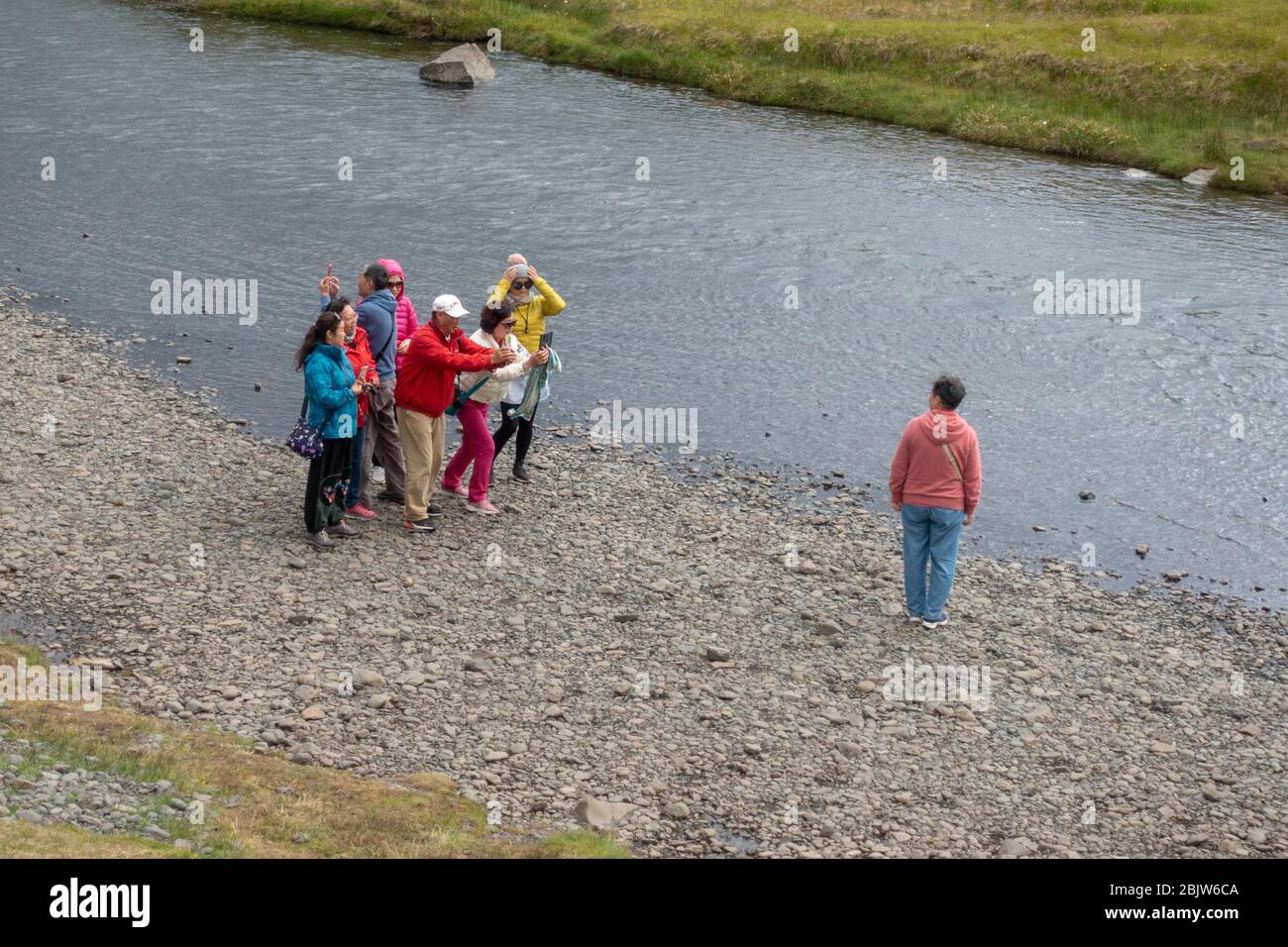 Un gruppo di turisti che si posa per fotografie vicino alla cascata di Kirkjufellsfoss e Kirkjufell ('Chiesa di montagna'), penisola di Snæfellsnes, Islanda. Foto Stock