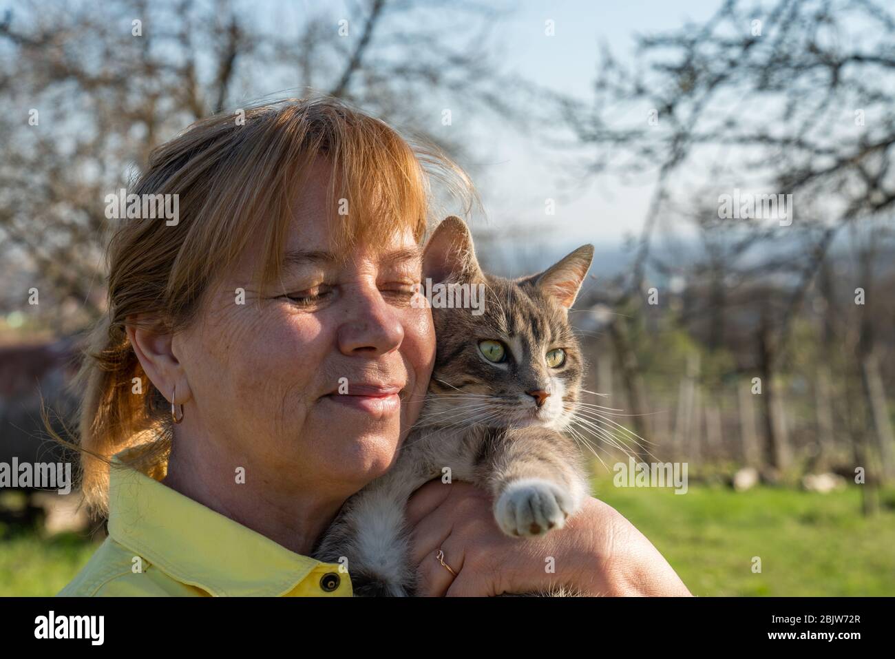 Donna con occhi chiusi che abbracciano il suo gatto grigio Foto Stock