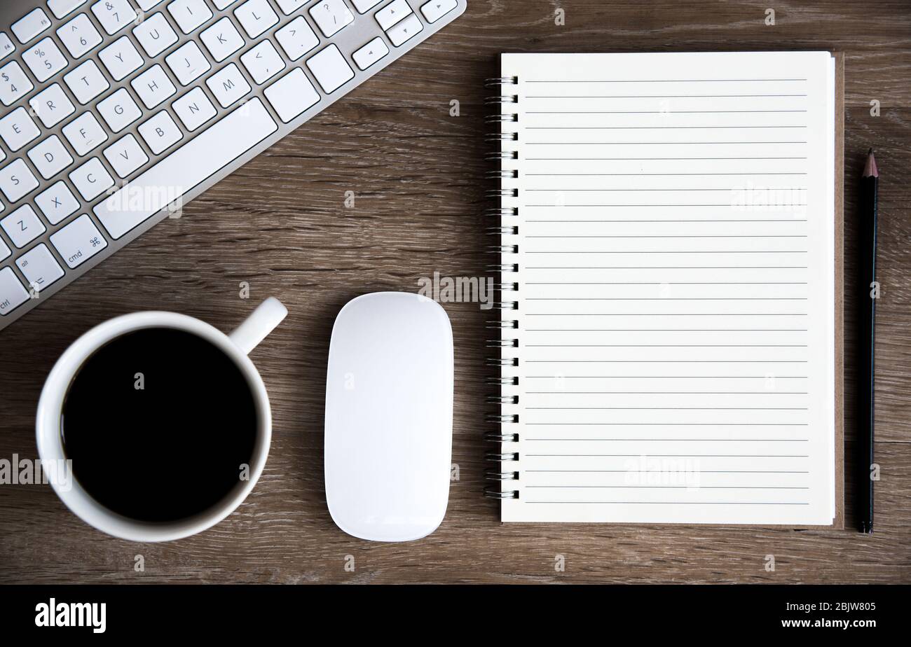 Una vista ad angolo elevato di una scrivania da ufficio con tastiera, caffè, mouse e notebook a spirale con spazio per le copie foderato per le note Foto Stock