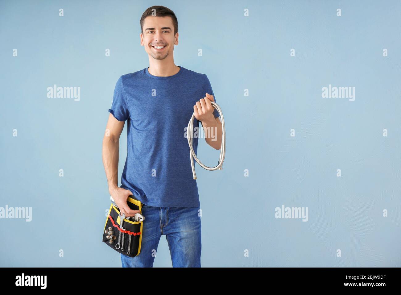 Idraulico giovane con cintura portautensili e tubo flessibile su sfondo colorato Foto Stock