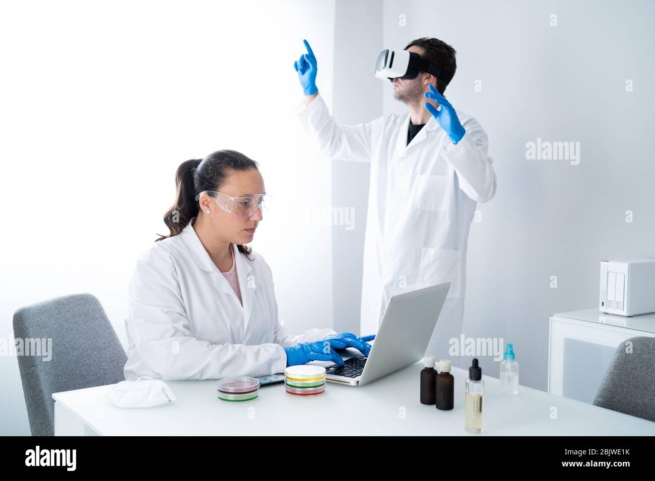 Giovani scienziati o ricercatori che lavorano nel moderno laboratorio di scienze biologiche. Donna lavora con campioni in un piatto di Petri e l'uomo è indossato Foto Stock
