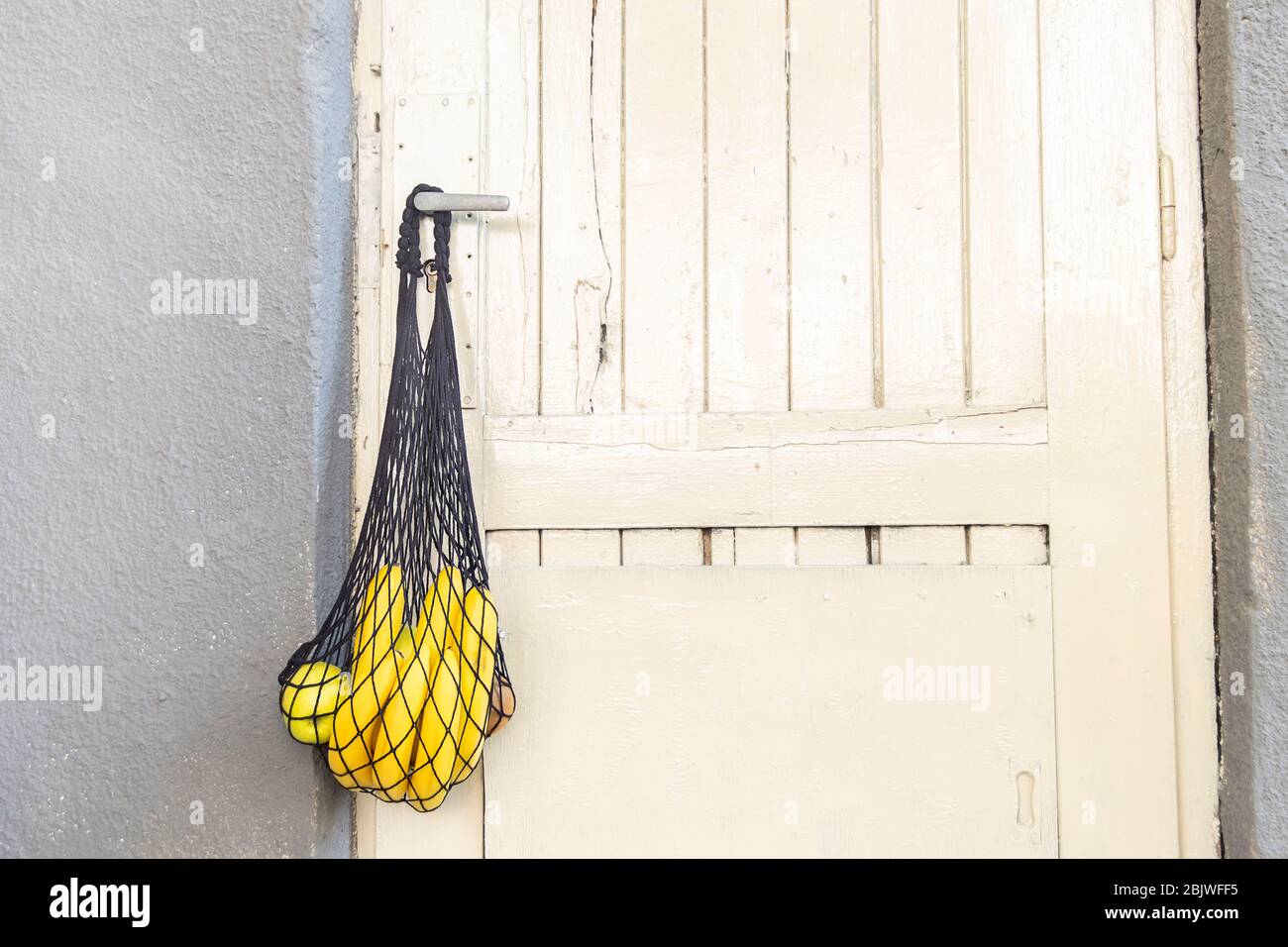 Somministrazione a domicilio durante la quarantena a causa dell'infezione da coronavirus COVID-19. Borsa con spesa con prodotti alimentari appesi sulla maniglia della porta Foto Stock