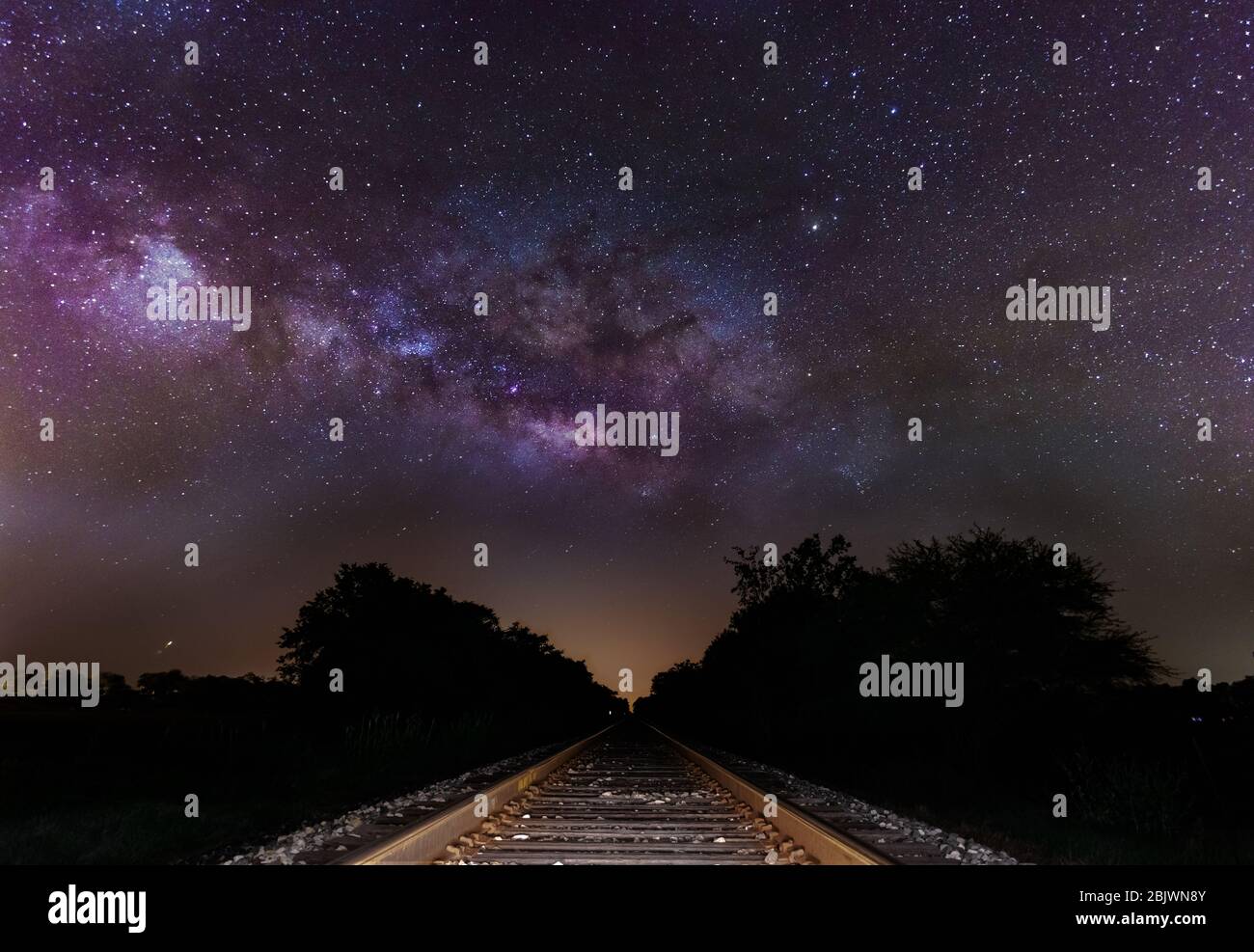 Milky Way si anima sulle piste del treno. Nucleo galattico che sorge maestosamente su binari ferroviari abbandonati in un campo rurale. Foto Stock