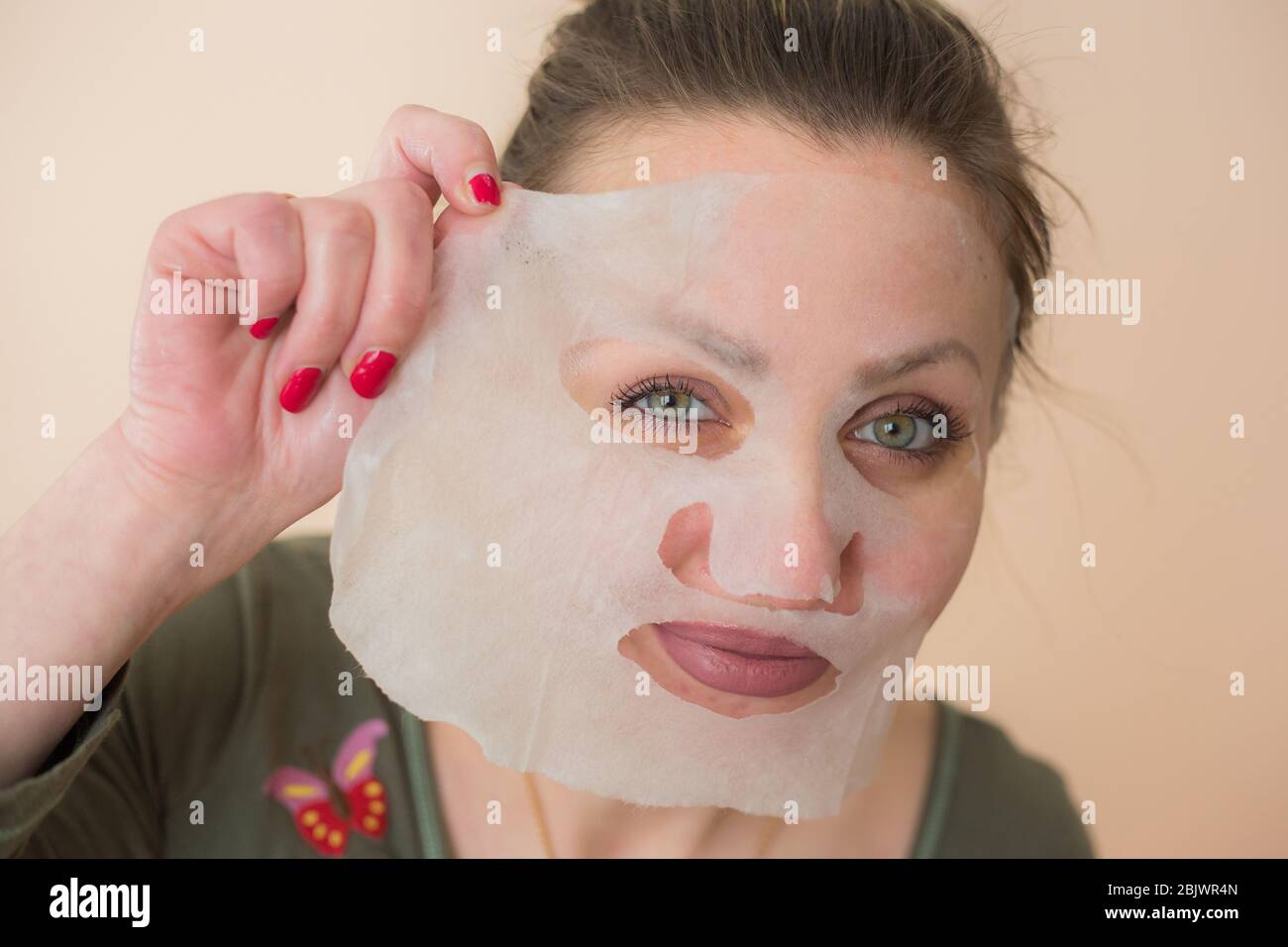 Maschera facciale cosmetica e ragazza guardare nello specchio Foto Stock