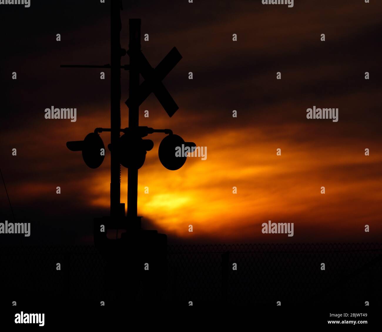 Una silhouette di un segnale e di un segnale di attraversamento ferroviario prima di un vibrante tramonto arancione. Foto Stock