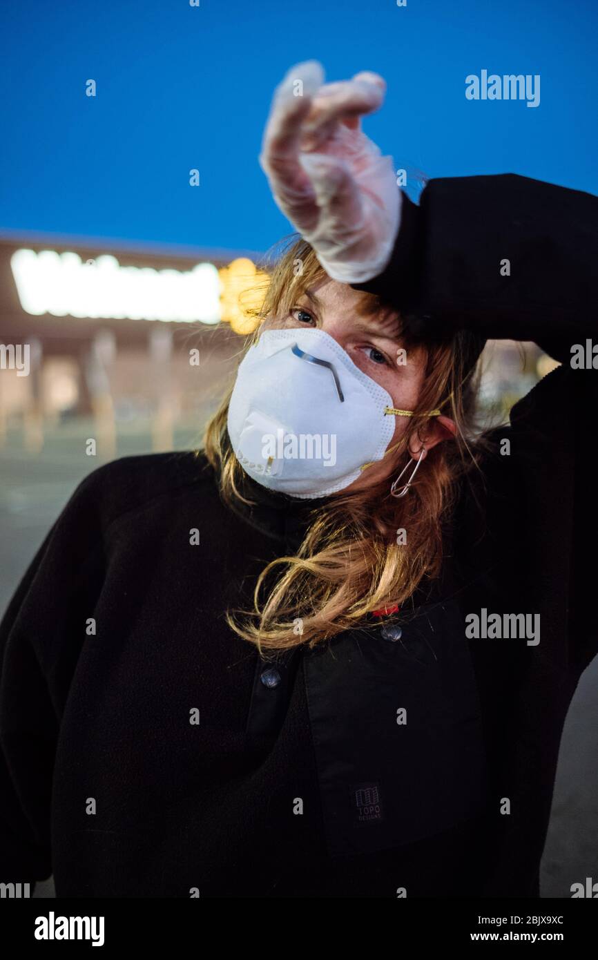 Una donna che indossa una maschera facciale PPE e guanti al di fuori di un negozio di alimentari durante la pandemia globale Covid-19. Foto Stock