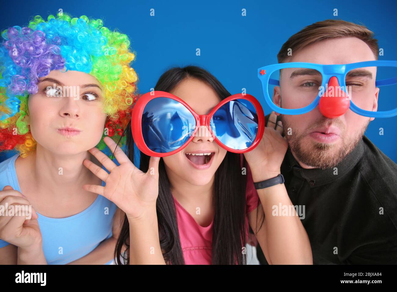 Giovani in divertente travestimento posa su sfondo colore. Festa dello sciocco di aprile Foto Stock