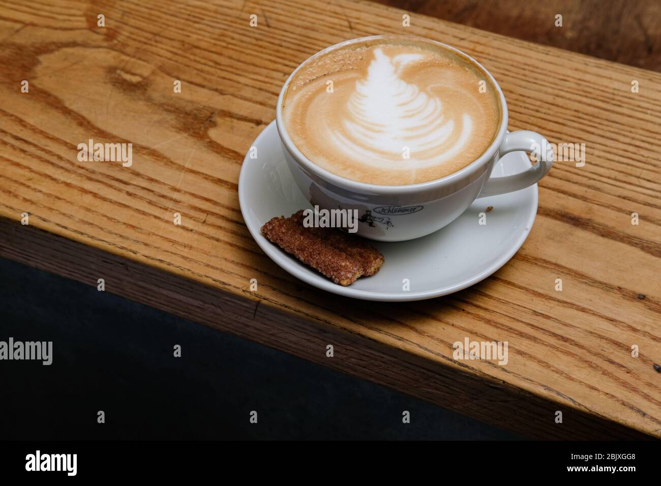 Tazza calda di cappuccino con bella latte art e biscotti su tavolo di legno, per colazione. Modello latte. Foto Stock