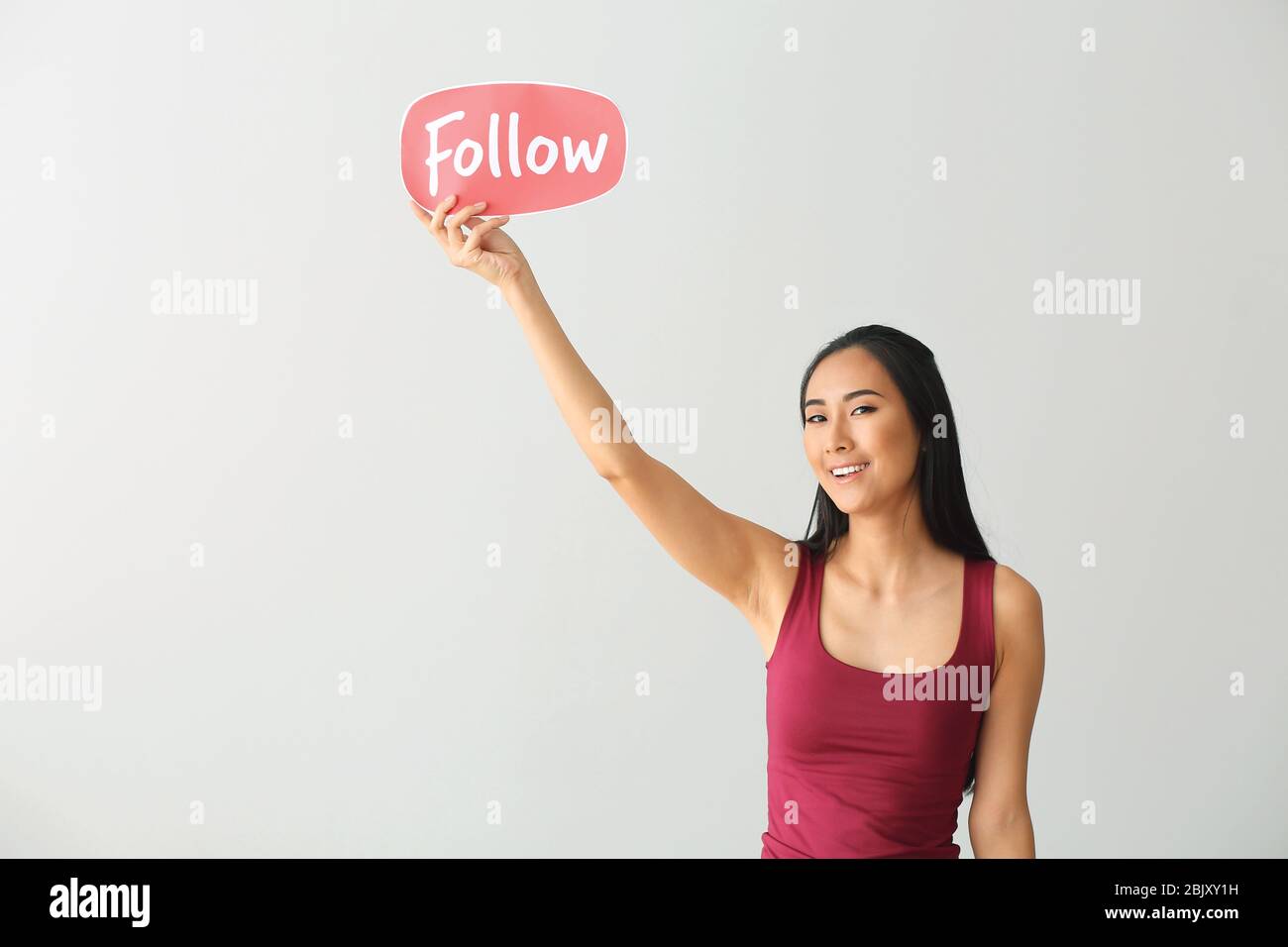 Femmina blogger asiatici tenendo la carta con seguire il testo su sfondo chiaro Foto Stock